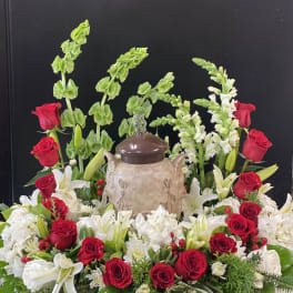 Red roses and white lilies arranged around a decorative urn on a black background.
