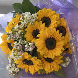 Bouquet of yellow sunflowers with small white blossoms wrapped in purple paper