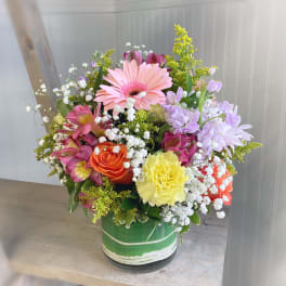 Mixed bouquet with pink gerbera, roses, carnations, and lavender blooms in a green vase
