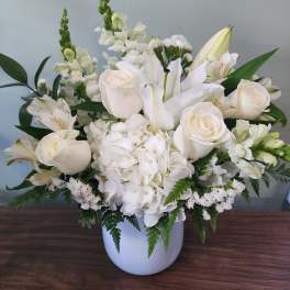 White floral arrangement in a white vase with roses and lilies