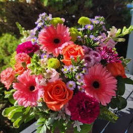 Bright mixed bouquet with pink gerbera daisies, orange roses, and purple accents in a wooden box