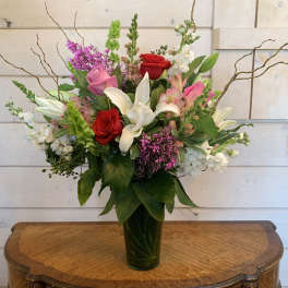 Mixed bouquet of roses, lilies, and pink flowers in a glass vase