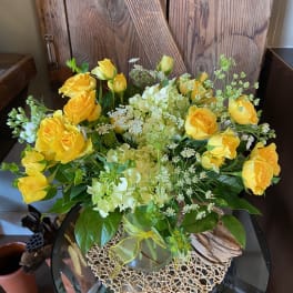 Medium arrangement of yellow roses and pale green hydrangeas in a clear glass vase