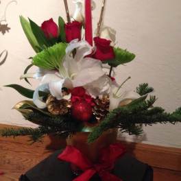 Red roses and white lilies in a holiday arrangement with pinecones and a red candle.