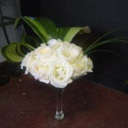 White rose bouquet in a clear glass vase with large green leaves