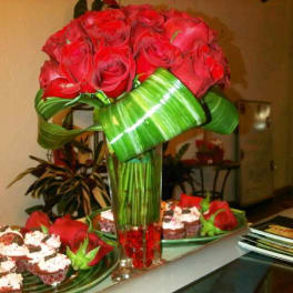 Red rose arrangement in a tall glass vase with green ribbon wrap