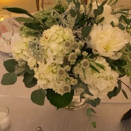 White floral centerpiece in a clear glass vase with eucalyptus