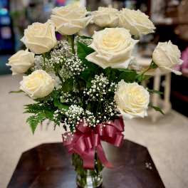 Cream roses in a glass vase with baby's breath and a pink ribbon