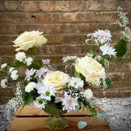 Cream roses and white daisies in a clear vase with pastel filler flowers