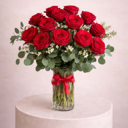 Red roses arranged in a clear glass vase with a red ribbon