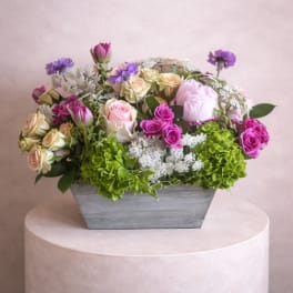 Mixed roses and purple flowers in a gray rectangular vase