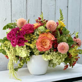 Mixed bouquet of pink, peach, and green flowers in a white pot