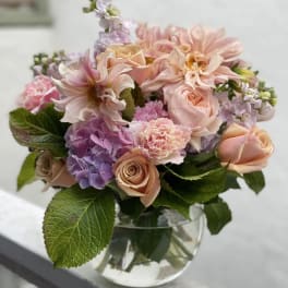 Low glass vase of peach roses, pink dahlias, and purple hydrangea with lush foliage