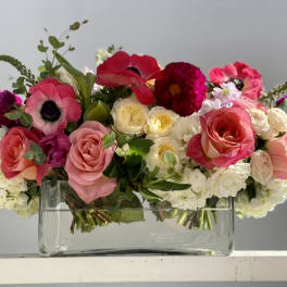Low rectangular arrangement of pink, red, and white flowers in a clear glass vase