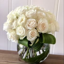 White rose bouquet in a clear glass vase with broad green leaves