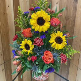 Tall mixed bouquet with sunflowers, roses, and carnations in a decorative vase