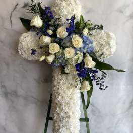 White floral cross on a stand with cream roses and blue flowers
