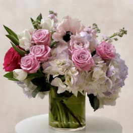 Pink roses, white tulips, anemones, and pastel hydrangeas in a clear glass vase