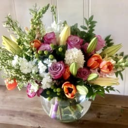 Mixed bouquet of roses, lilies, and tulips in a glass bowl vase