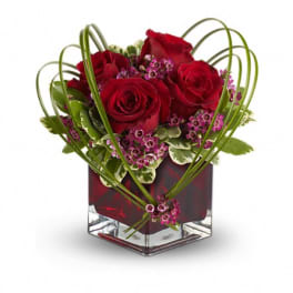 Red roses and pink filler flowers in a square glass vase
