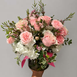Pink roses and white hydrangeas in a glass vase with a pink ribbon