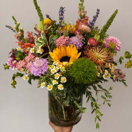 Mixed bouquet with a sunflower, daisies, and pink blooms in a glass vase