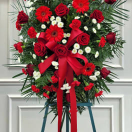 Red roses and gerbera daisies in a standing spray with a red ribbon