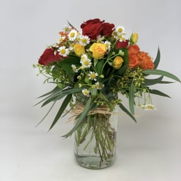 Mixed bouquet of red and yellow roses with white daisies in a glass vase
