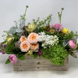 Low garden-style arrangement of mixed pastel flowers in a rustic wooden box