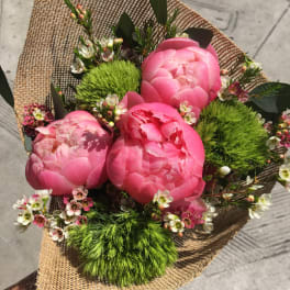 Pink peony bouquet with small white blossoms wrapped in burlap