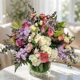 Mixed bouquet of pink, white, and lavender flowers in a clear glass vase