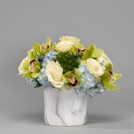 White roses and blue hydrangeas in a white vase with green orchids