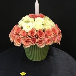 Pink and white rose arrangement in a green vase with a white candle