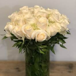Cream roses arranged in a glass vase with dark green foliage