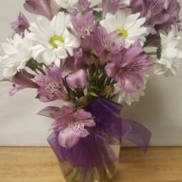 White daisies and purple alstroemeria in a glass vase with a purple ribbon
