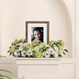 White and green funeral arrangement with a framed portrait in the center