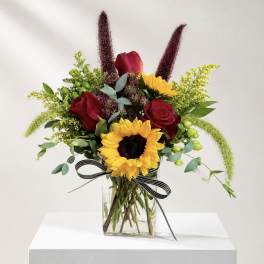 Bouquet of red roses and sunflowers in a glass vase with a striped ribbon