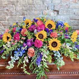 Colorful floral casket spray with sunflowers, roses, and purple blooms
