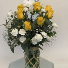 Yellow roses and white carnations in a glass vase with a butterfly pick