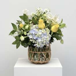 Yellow roses and blue hydrangeas in a glass vase with woven wrap