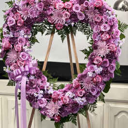 Heart-shaped pink and purple floral wreath on an easel with a ribbon bow