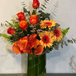 Orange roses, calla lilies, and yellow gerbera daisies in a glass vase