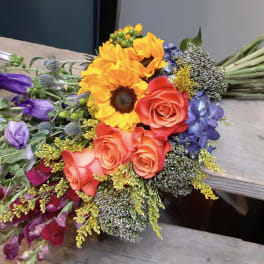 Colorful bouquet with sunflowers, roses, and purple blooms on a bench