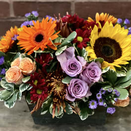 Mixed bouquet with sunflowers, roses, and gerbera daisies in a dark container