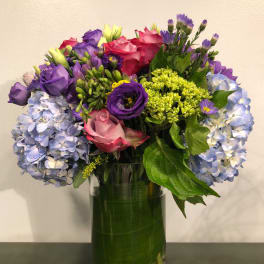 Mixed bouquet of roses, hydrangeas, and purple flowers in a glass vase
