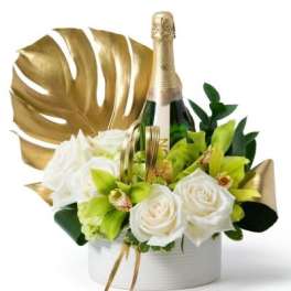 White roses and green orchids arranged around a champagne bottle with gold accents in a white container
