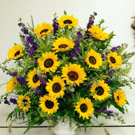 Bright sunflower arrangement in a white vase with purple accents