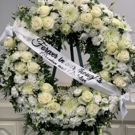 White floral funeral wreath with a memorial ribbon on an easel