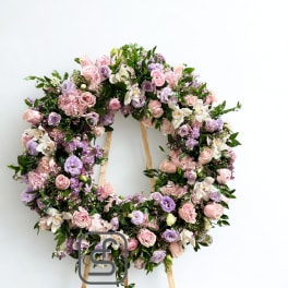 Standing wreath of pink and lavender roses and lisianthus on a wooden easel against a white background