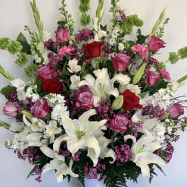Large bouquet of white lilies, pink and red roses, and purple filler flowers in a white vase